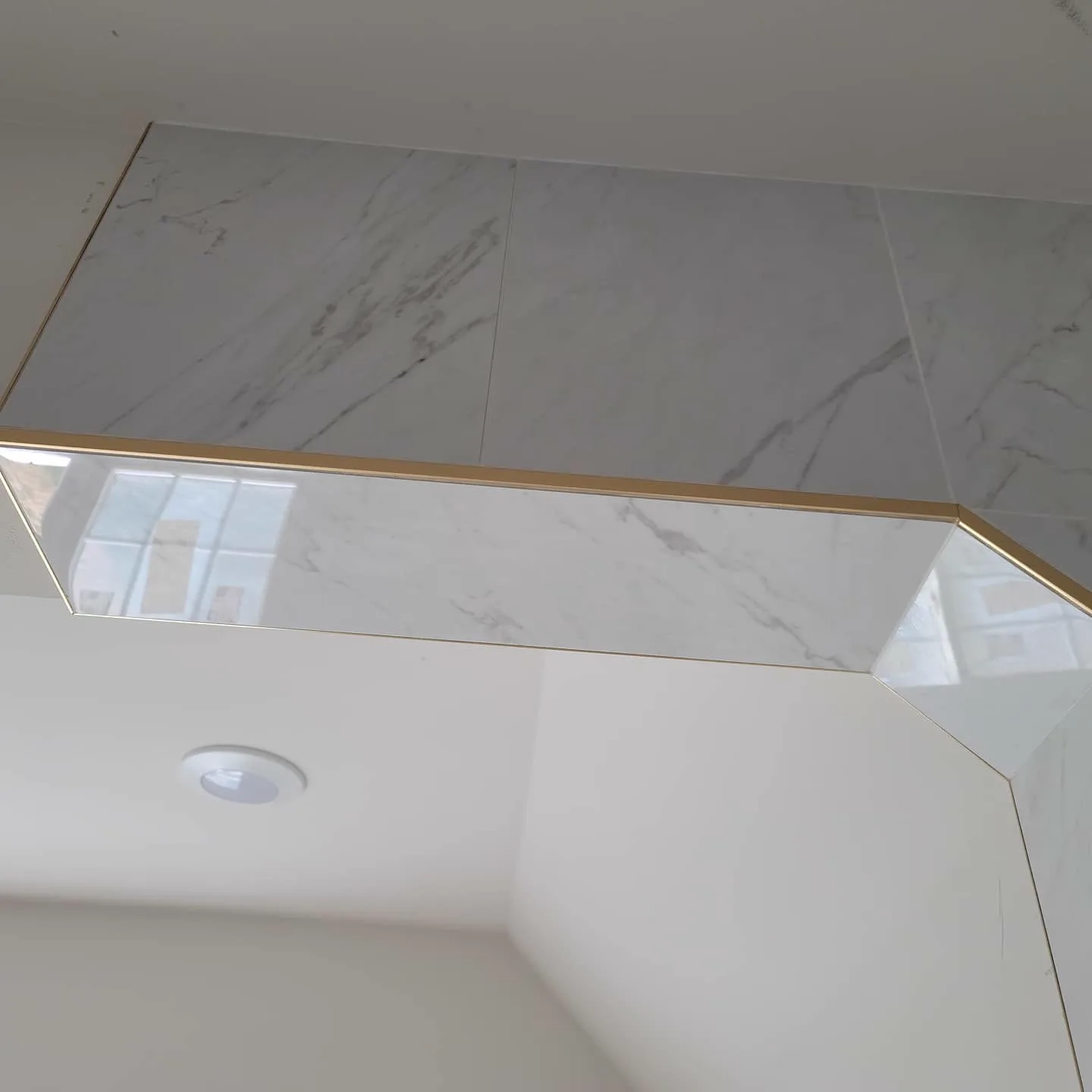 Marble shower corner detail beside a glass stair railing