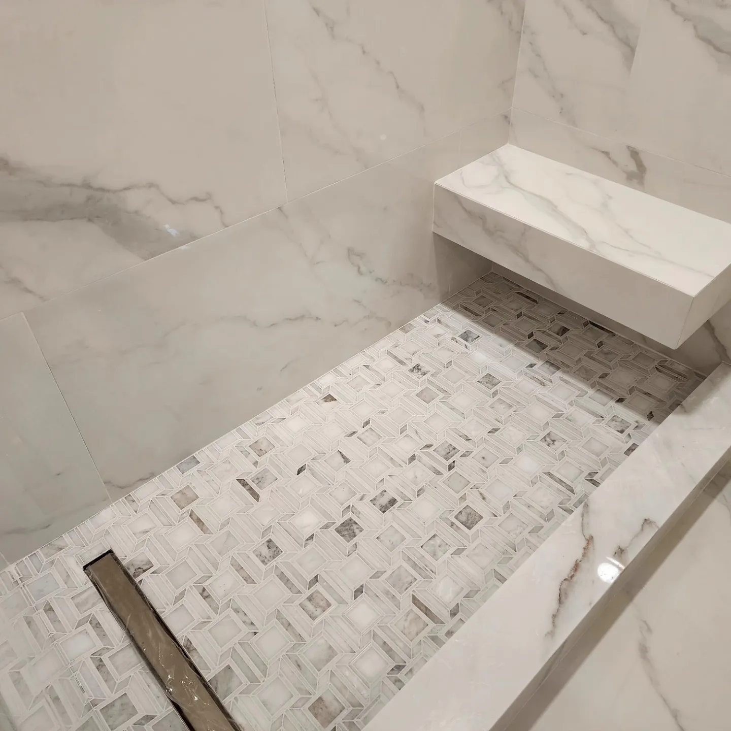 Marble shower with floating bench and geometric mosaic floor